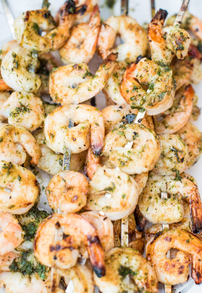 cooked honey cajun shrimp skewers with charred tails and an herb sauce brushed on top