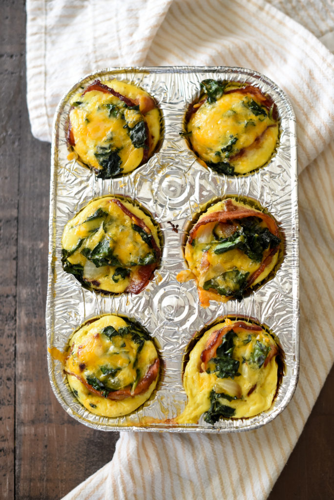 Grilled Egg Cups perfect for a summer meal prep: Light fluffy eggs, stuffed w/ greens, caramelized onions, & cheese wrapped in a piece of bacon. 