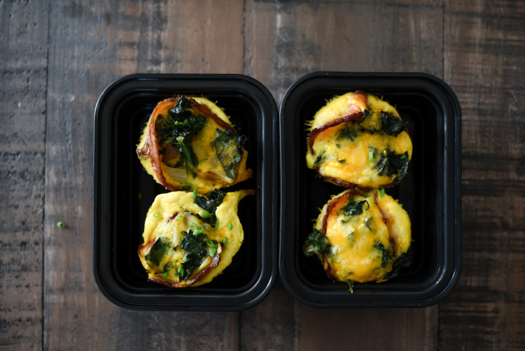 Grilled Egg Cups perfect for a summer meal prep: Light fluffy eggs, stuffed w/ greens, caramelized onions, & cheese wrapped in a piece of bacon. 