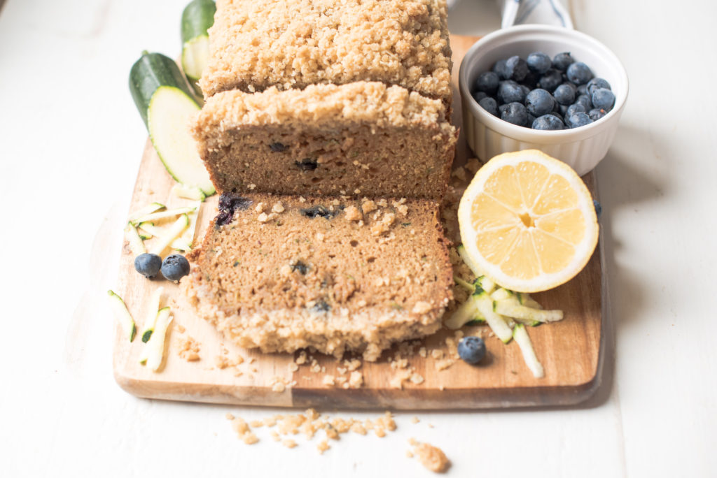 loaf of zucchini bread sliced on a wooden cutting board on top of a white table