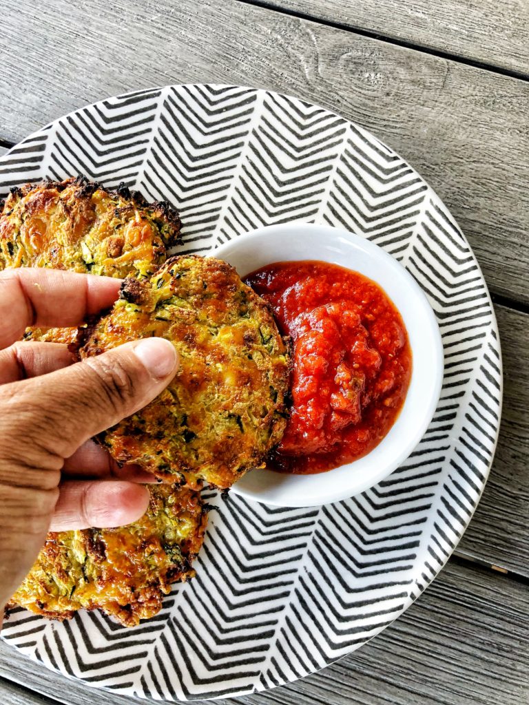 Zucchini fritters being dipped into marinara sauce 